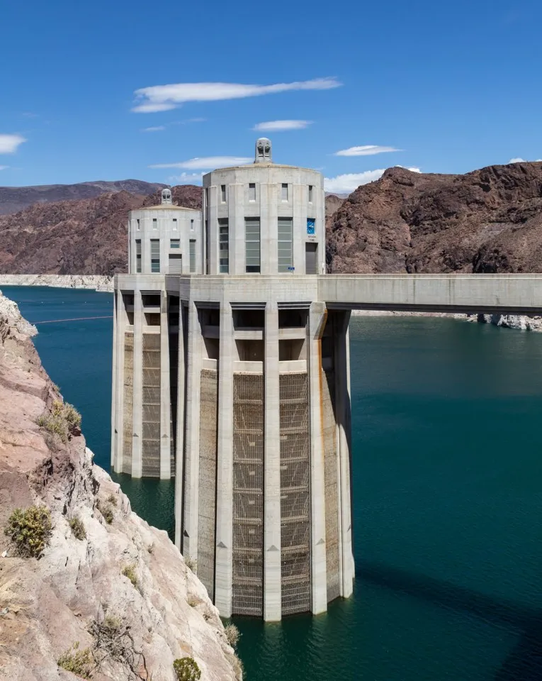 A pale concrete intake tower beside blue water and rocky slopes at Hoover Dam.