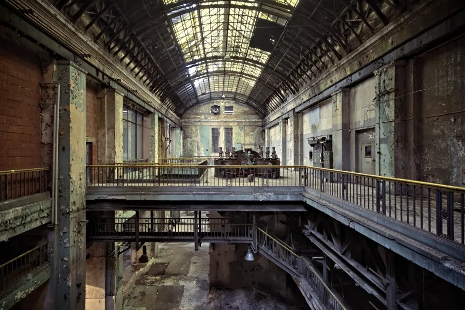 A vaulted industrial hall with steel walkways, weathered walls and a glazed roof.